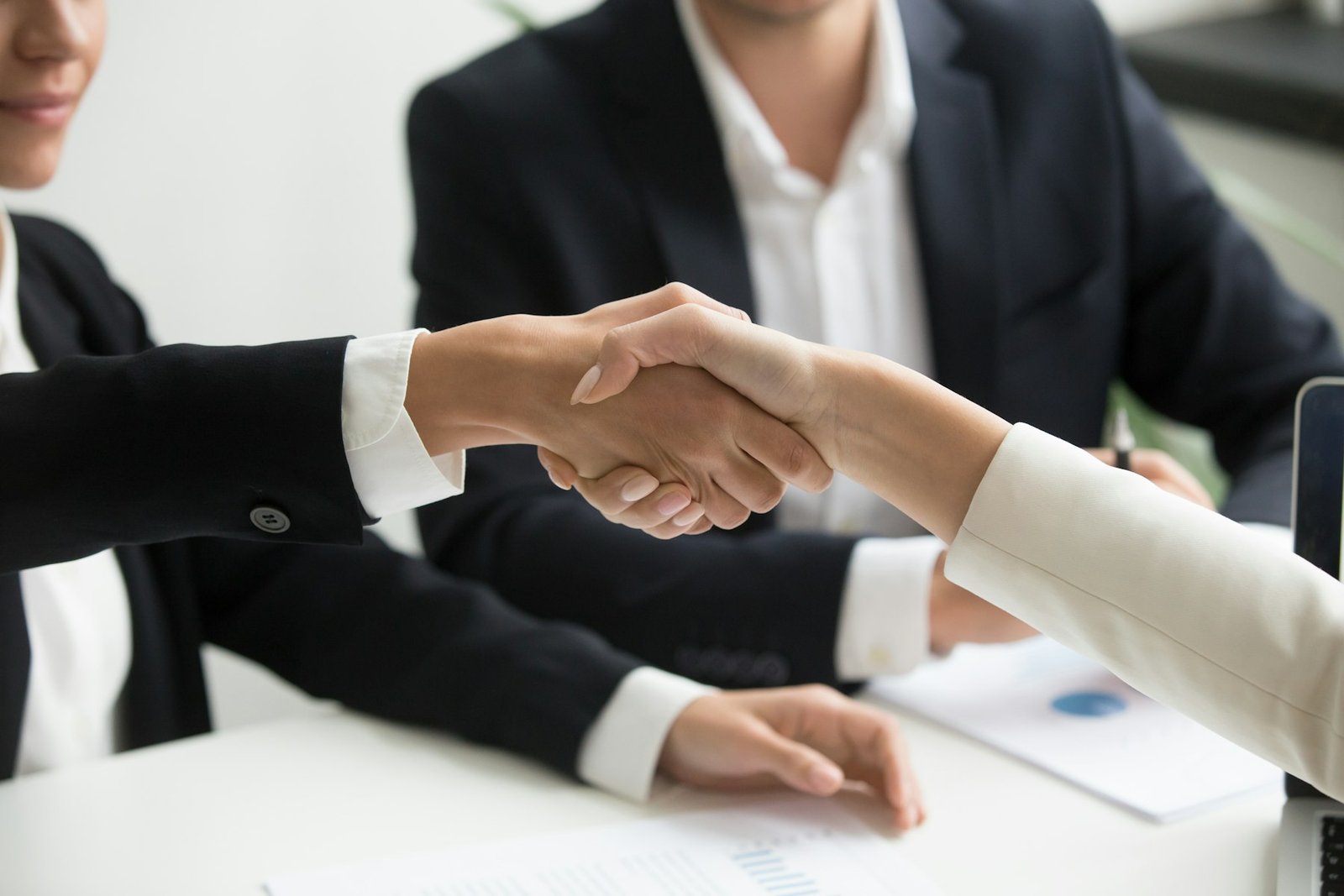 Two people shaking hands across a desk with a laptop